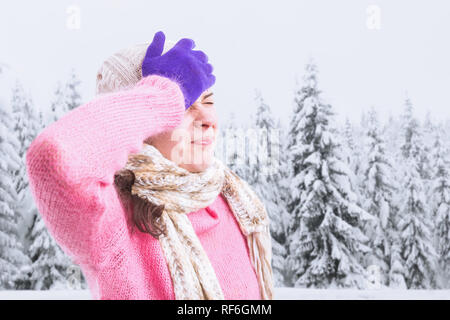 Donna con emicrania toccando la fronte con la mano indossando guanti viola come canna fumaria concetto di stagione in stagione invernale sullo sfondo del paesaggio Foto Stock
