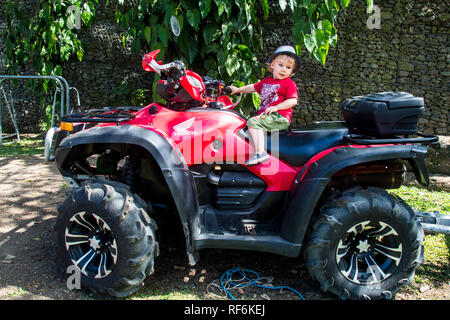 La foto di un bambino di 2 anni bambino seduto su un rosso Honda ATV, San Jose, Costa Rica Foto Stock