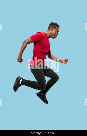 Libertà di movimento e il moto in avanti. La felice sorpresa del giovane africano saltare un contro blu di sfondo per studio. Runnin uomo in movimento o movimento. Le emozioni umane e le espressioni del viso Foto Stock