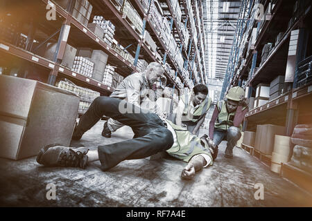 I lavoratori facendo attenzione circa il loro collega sdraiato sul pavimento Foto Stock