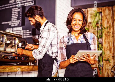 Cameriera utilizzando un computer tablet e cameriere con macchina per il caffè Foto Stock