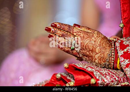 Tradizionali gioielli nuziale e decorazione henné sulle mani della sposa durante una cerimonia religiosa a nozze indù Foto Stock