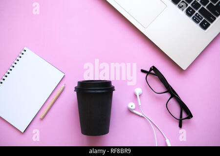 Area di lavoro in un quartiere alla moda di colore rosa. Molte cose diverse tra cui un computer portatile e le cuffie sono sul tavolo. Foto Stock