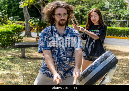 Un insegnante e uno studente gioca un giapponese taiko tamburo fatto di un vecchio pneumatico e nastro adesivo. Fotografato in un bellissimo parco verde. Foto Stock