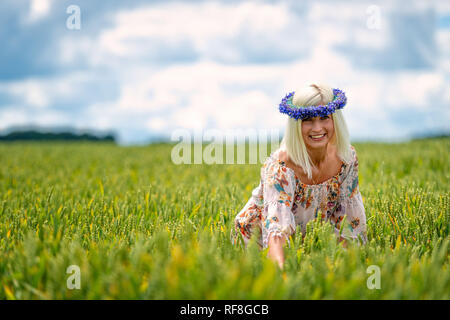 Bella e suggestiva, donna bionda con blu fiordaliso crown nel settore dei cereali. Foto Stock