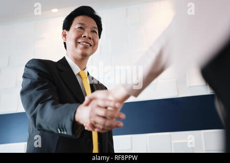 Stretta di mano tra felice Asian Manager e imprenditrice ispanica in Office Foto Stock