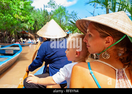 La famiglia felice corsa sulla tradizionale vietnamita barca dal giallo bruno acqua nel canale. Il fiume Mekong Delta - Saigon popolare destinazione di viaggio Foto Stock