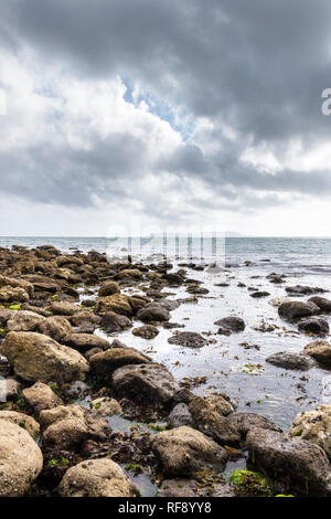 Nuvole temporalesche raccolta su una spiaggia rocciosa nel Dorset, sud ovest dell'Inghilterra, Regno Unito, Portland Bill in lontananza Foto Stock