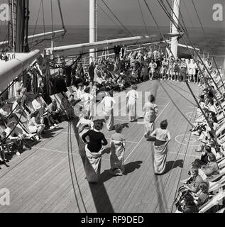 Degli anni Cinquanta, storico fuori in mare a bordo di un battello a vapore Union-Castle voce per il capo in Sudafrica, femmina i passeggeri che prendono parte a un sacco di gara sul ponte, guardato dall'altra nave i viaggiatori, alcuni seduti in sedie a sdraio. Foto Stock