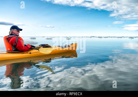 SVALBARD, Norvegia: Un kayak pedala attraverso le calme e ghiacciate acque dell'Oceano Artico, circondato da piccole banchine di ghiaccio sotto un cielo azzurro. L'attività offre un'esperienza immersiva nell'ambiente incontaminato dell'Artico, mettendo in evidenza i suoi paesaggi glaciali unici e i fragili ecosistemi. Le Svalbard, un arcipelago situato nell'Oceano Artico, sono note per il loro paesaggio spettacolare, i ghiacciai e l'abbondante fauna selvatica, che lo rendono una destinazione popolare per il turismo avventuroso. Foto Stock