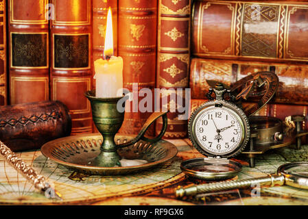 Vintage orologio da tasca e candela che brucia in un vecchio candelabro sono sullo sfondo dei libri antichi Foto Stock