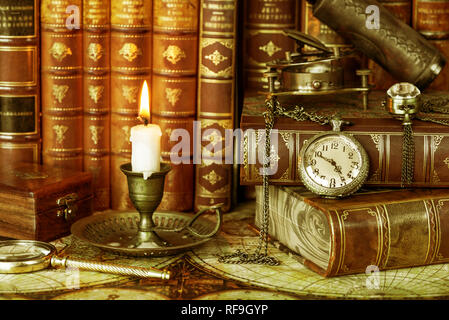 Vintage orologio da tasca e candela che brucia in un vecchio candelabro sono sullo sfondo dei libri antichi Foto Stock