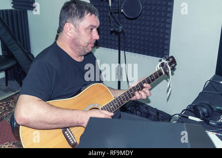 Barba lunga, big man a home studio di registrazione con chitarra in mano, foto naturale Foto Stock