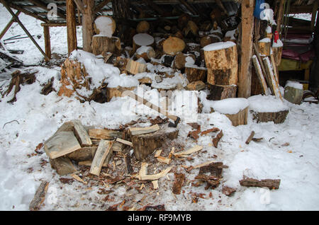 Vecchio arrugginito ax bloccato in un legno secco log.ceppi di alberi impilati in background. Foto Stock