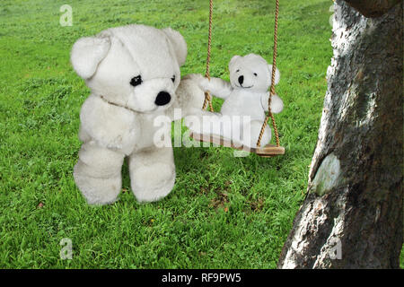 Adulto orsacchiotto dando cub bambino una mano con lo swing nel parco giochi Foto Stock