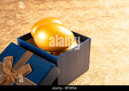 Uova di oro in un presente casella su sfondo dorato Foto Stock