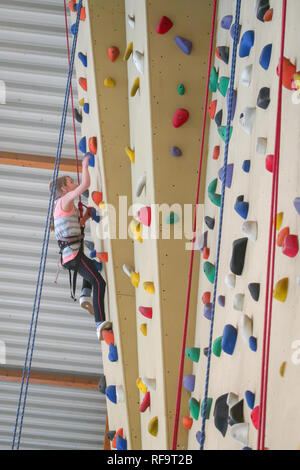 Un 9 anno vecchia ragazza si arrampica su una parete di arrampicata in una sporgenza Foto Stock