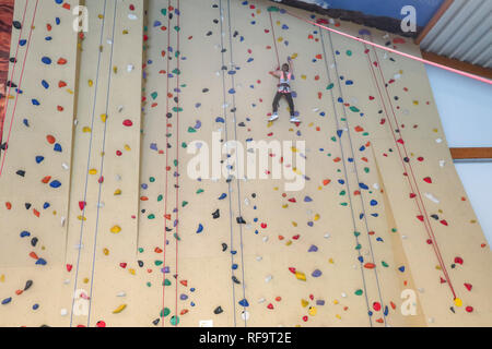 Un 9 anno vecchia ragazza si arrampica su una parete di arrampicata Foto Stock