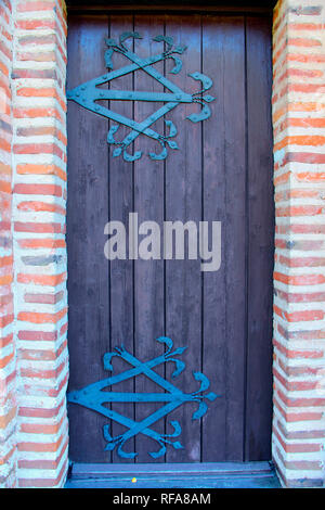 Antica porta di legno con ferro forgiato la cerniera. Vecchia chiesa porta che conduce al luogo religioso realizzato dal rosso mattone. Muro di mattoni rossi con la vecchia porta di legno Foto Stock