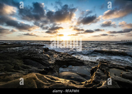 Onde che si infrangono sulla spiaggia rocciosa al tramonto Foto Stock