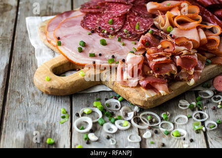 Mix di antipasti di carne - salame, prosciutto, tacchino affumicato, salsicce e prosciutto - rustico sfondo di legno Foto Stock