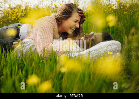 Interracial giovane giacente su erba verde e ridere. Giovane uomo e donna sdraiata nel prato fiorito all'esterno. Foto Stock