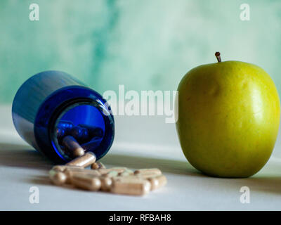 Un Apple e un contenitore blu con fibre vegetali pillole su un tavolo Foto Stock