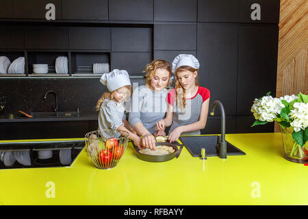 La famiglia felice in cucina. Madre e due bambini di preparare la pasta di pane, cuocere la torta di mele. La mamma e le figlie per la cottura di alimenti sani a casa e divertirsi. Casa Foto Stock