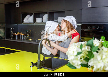 Due ragazze con chef hat abbracciando e divertirsi in cucina. Sorelle piccolo ragazzo e ragazza adolescente per la cottura di alimenti sani a casa. Infanzia e famiglia, househ Foto Stock