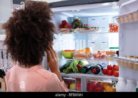 Vista posteriore di una donna confusa alla ricerca di cibo in un frigorifero aperto Foto Stock