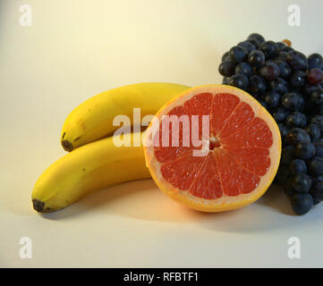 Un mazzetto di mature, gustose banane, tre pezzi, un grappolo di uva e la metà di un pompelmo mature. La foto è stata scattata in lightbox, close-up. Foto Stock
