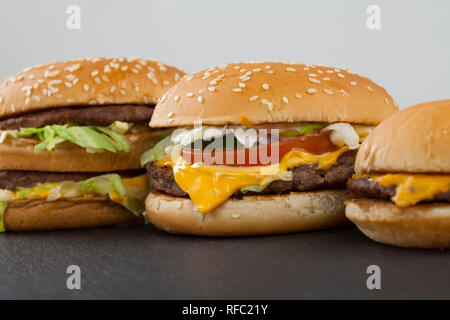 Tre diverse tipologie e dimensioni di deliziose cheeseburger su un piatto nero e sfondo bianco Foto Stock