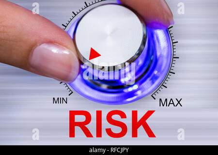 La mano di una persona che riduce al minimo il rischio pulsante regolatore su sfondo grigio Foto Stock