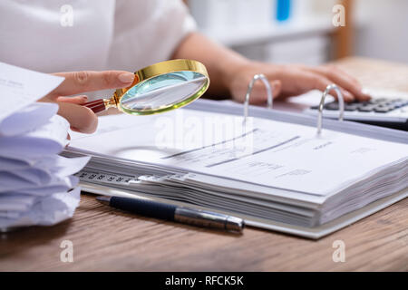 Close-up di una imprenditrice la mano che tiene la lente di ingrandimento su fattura al posto di lavoro Foto Stock