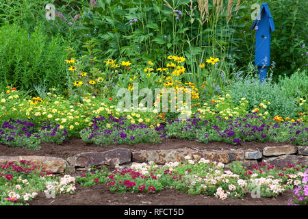 63821-21817 giardino fiorito con muro di pietra e blue bird house. lampone blast e petunia diamond frost euphorbia in blu pot, Butterfly boccole, Peac Foto Stock