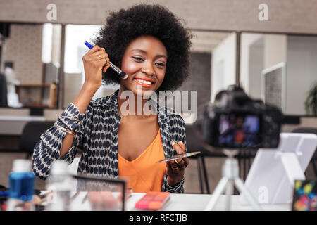 Bella americano africano donna con capelli ricci facendo prova di cosmetici Foto Stock