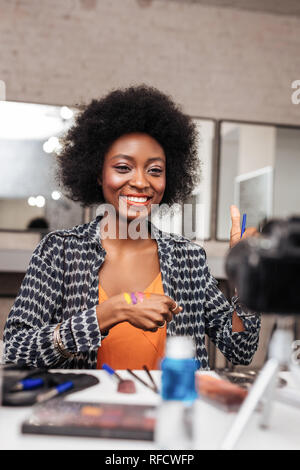 Bella donna con capelli scuri, occhi brillanti e labbra dipinte di rosso  guardando con sicurezza e con sorriso alla macchina fotografica indossando cappello  di paglia e collana sul collo. Po Foto stock 