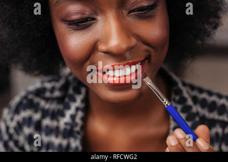 Incredibile americano africano donna con capelli ricci cercando un nuovo colore di rossetto Foto Stock