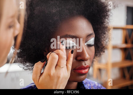 Biondo giovane stilista con nero smalto per unghie mettendo eyeshadows Foto Stock