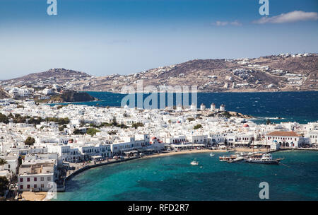 Vista panoramica della città di Mykonos harbour con famosi mulini a vento dalle colline sopra su una soleggiata giornata estiva, Mykonos, Cicladi Grecia Foto Stock