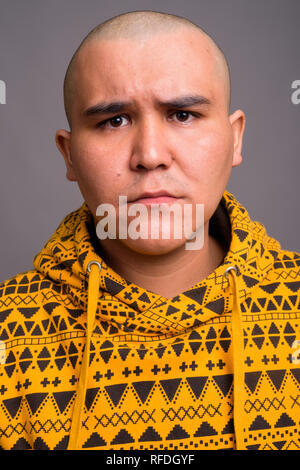 Giovani bald uomo asiatico contro uno sfondo grigio Foto Stock
