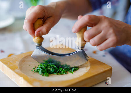 Una donna trita il prezzemolo su un tagliere di legno in cucina Foto Stock