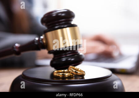 Primo piano della Golden gli anelli di nozze su mazzuolo di legno a tavola nelle aule di tribunale Foto Stock