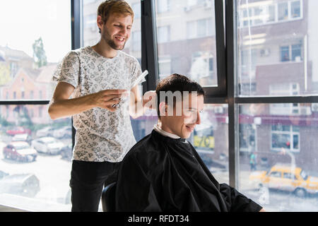 Parrucchiere non i capelli con il pettine di bello cliente soddisfatto in professional parrucchiere Foto Stock