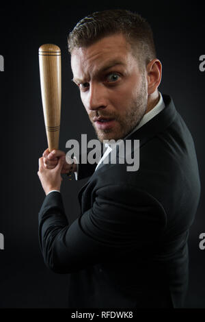 Imprenditore o un uomo in abito formale su sfondo scuro. Uomo sulla faccia di rigorosa in posa con la mazza di legno. Uomo con setola guarda fiducioso e minaccioso. Aggressivo il concetto di business. Foto Stock