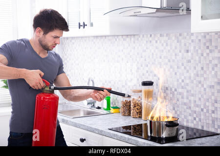 Uomo che utilizza un estintore per arrestare il fuoco sulla masterizzazione di pentola di cottura in cucina Foto Stock