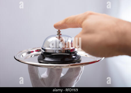 Close-up di persona la mano di servizio chiamata campana sulla piastra DETENUTE DA CAMERIERE Foto Stock