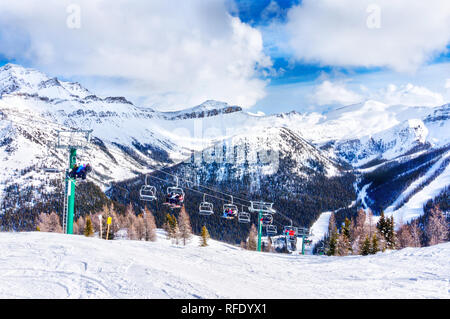 Identificabili gli sciatori e gli snowboarder sulla seggiovia andando su una pista da sci in montagna innevata gamma delle Canadian Rockies. Foto Stock