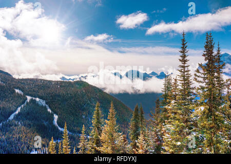 Mattina picchi di sole attraverso le nuvole basse sopra il nevoso inverno paesaggio di montagna del lago Louise nelle Montagne Rocciose Canadesi vicino al Parco Nazionale di Banff, Canada. Foto Stock