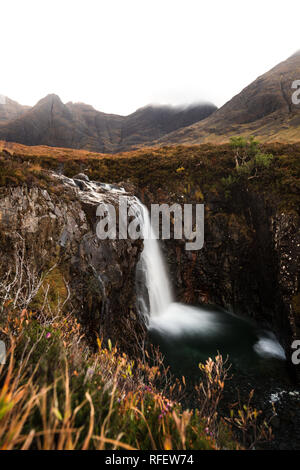 Pittoresca cascata presso la fata di piscine con coperto nebbia montagne sullo sfondo ed erba come primo piano (Isola di Skye in Scozia, Europa) Foto Stock